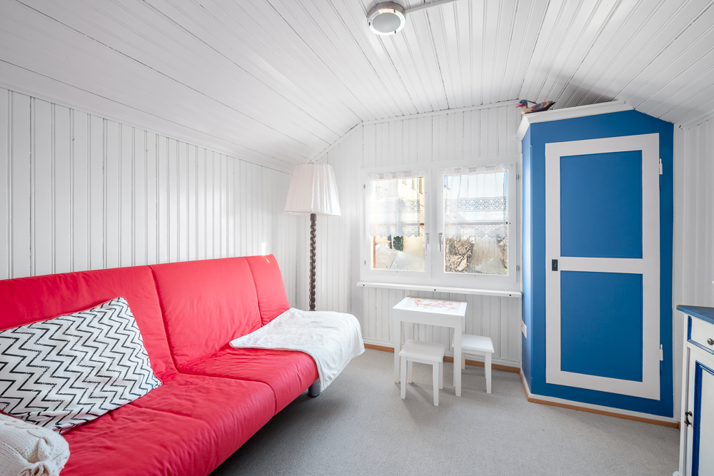 Heller kleiner Wohnraum mit rotem Sofa und blauer Tür