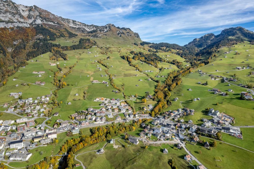 Luftaufnahme einer alpinen Ortschaft in grüner Berglandschaft