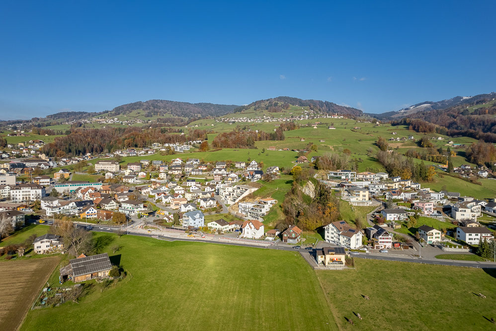 Luftaufnahme einer hügeligen Ortschaft mit Wiesen und Wohnbebauung
