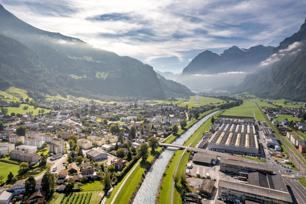 Luftaufnahme eines alpinen Tals mit Fluss, Stadt und Bergen
