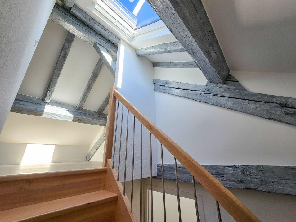 Treppenaufgang mit sichtbaren Holzbalken und Dachfenster