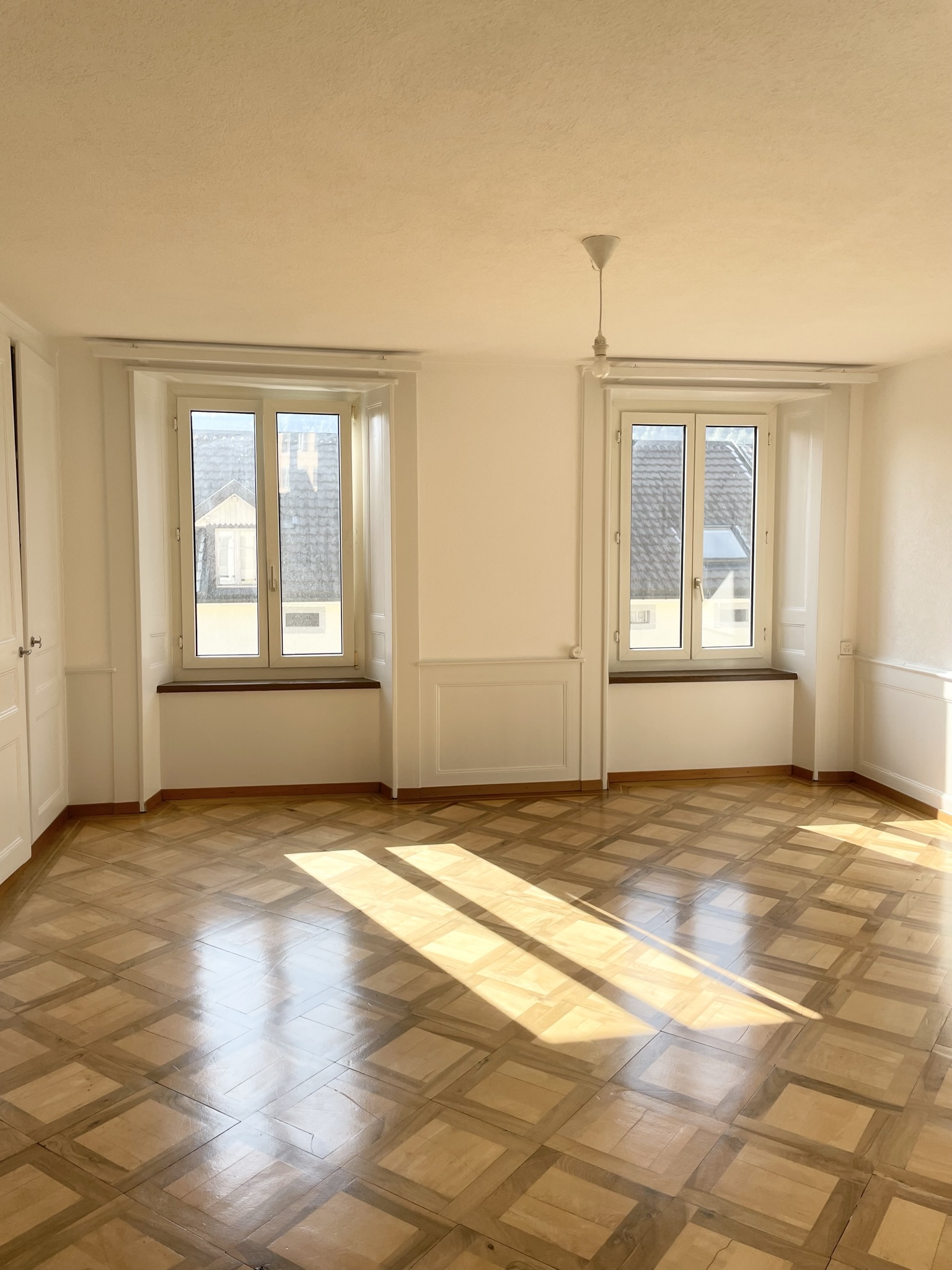 Heller leerer Wohnraum mit Parkettboden und zwei Fenstern