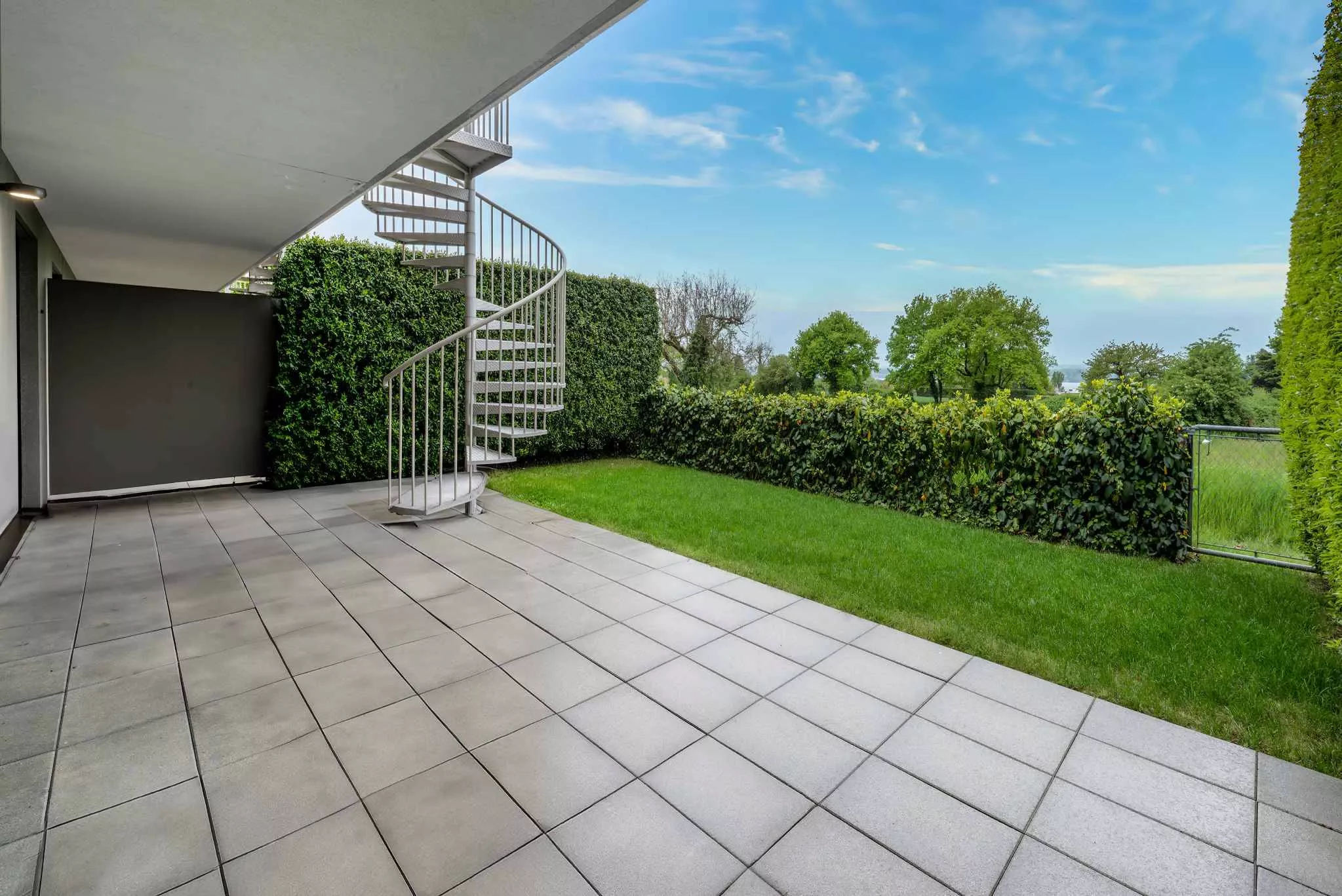 Überdachte Terrasse mit Wendeltreppe und Gartenblick