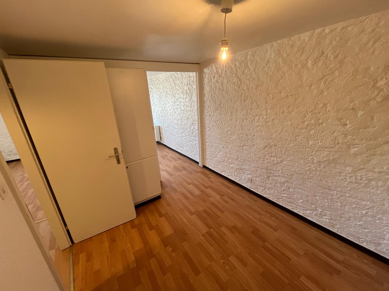 Schmaler Innenraum mit Holzboden und weißer Strukturwand