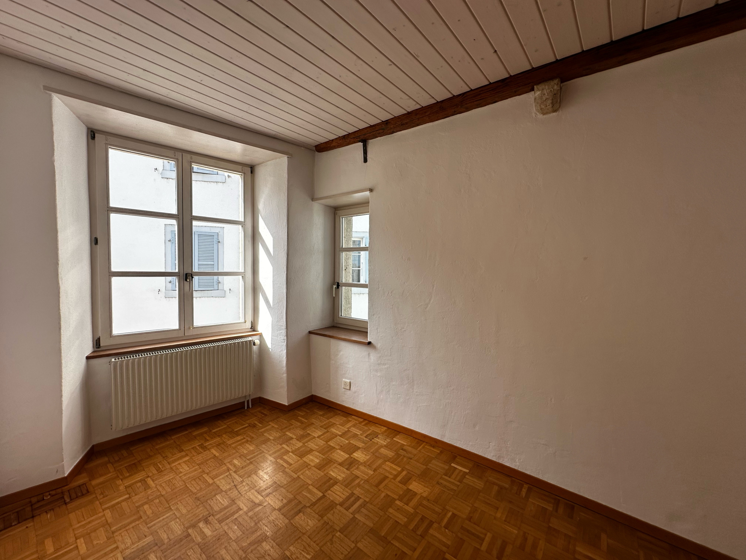 Leerer Altbau-Raum mit Parkett und Fenstern