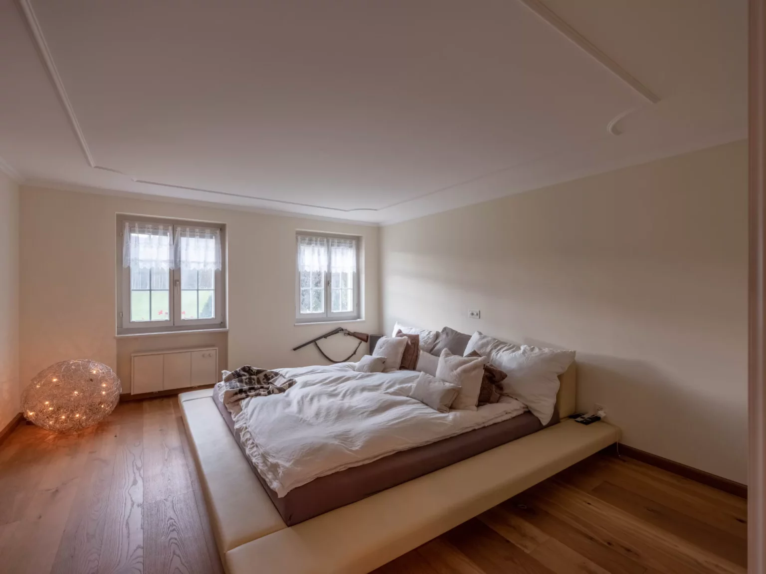 Helles Schlafzimmer mit niedrigem Bett und zwei Fenstern