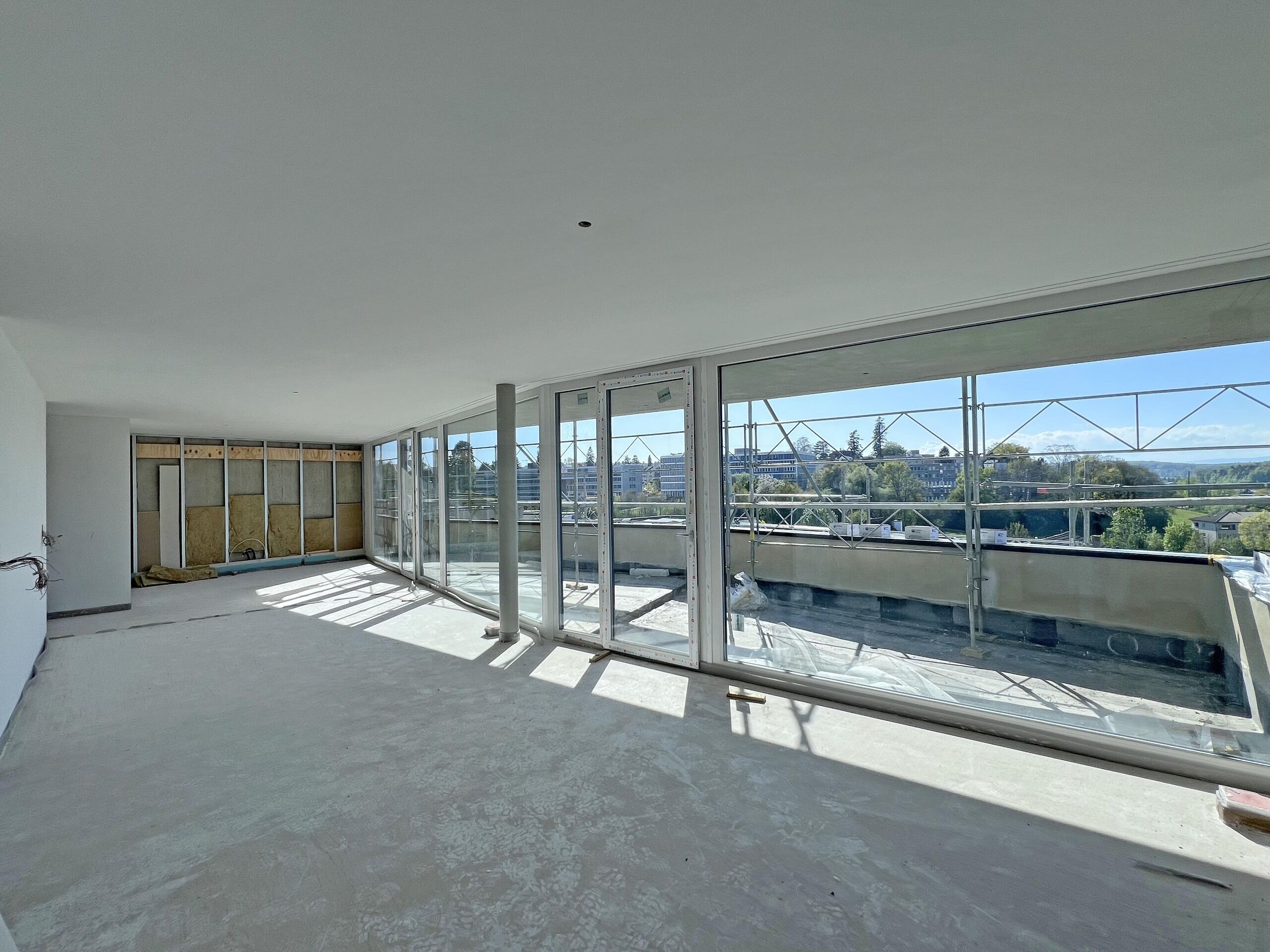 Großer Rohbau-Wohnraum mit bodentiefen Glasfronten und Balkonblick