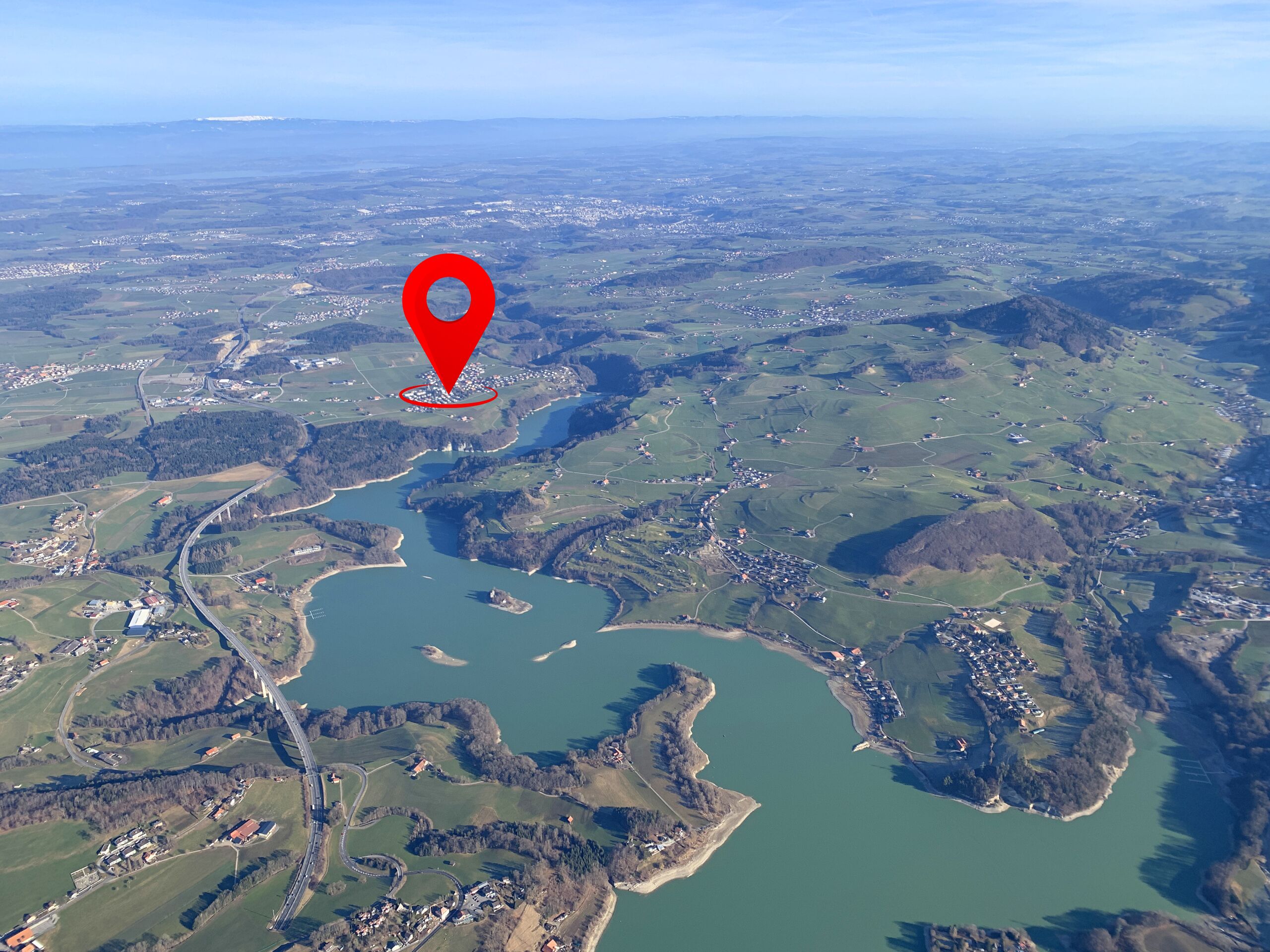 Luftaufnahme einer Landschaft mit See und Ortsmarkierung