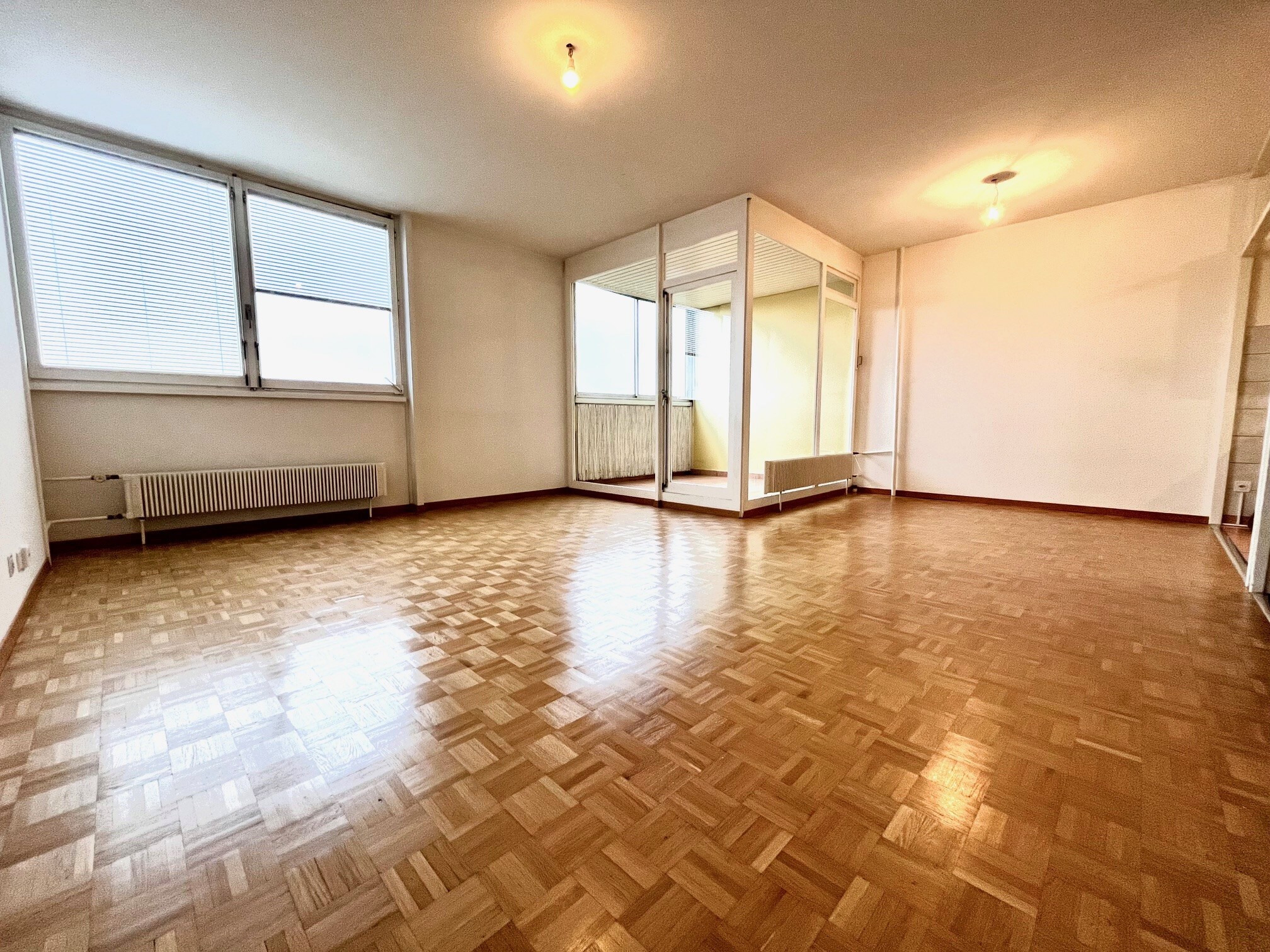 Leerer Wohnraum mit Parkett und großen Fenstern
