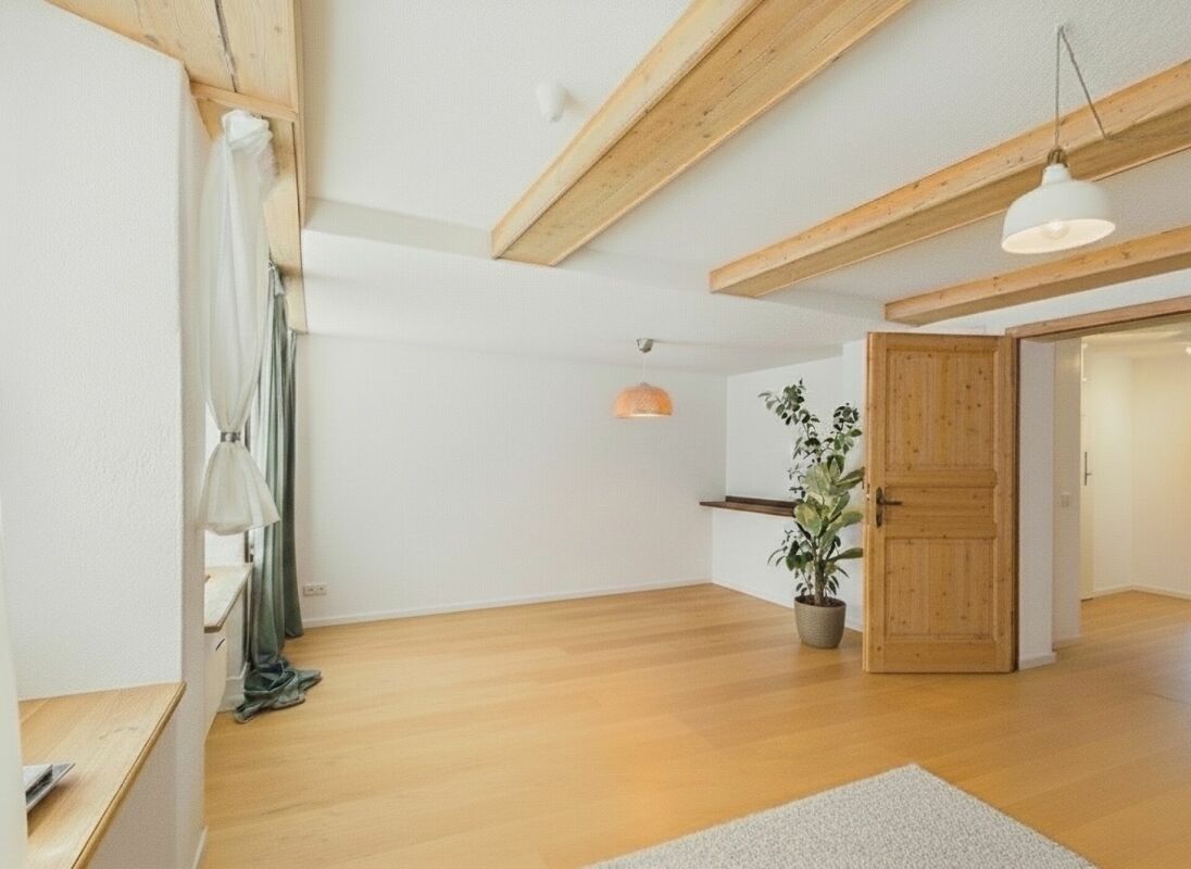 Helles, nahezu leeres Schlafzimmer mit sichtbaren Holzbalken