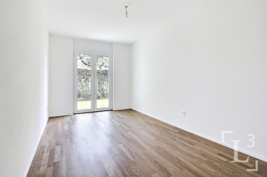 Leerer, heller Raum mit Holzfußboden und bodentiefen Fenstertüren