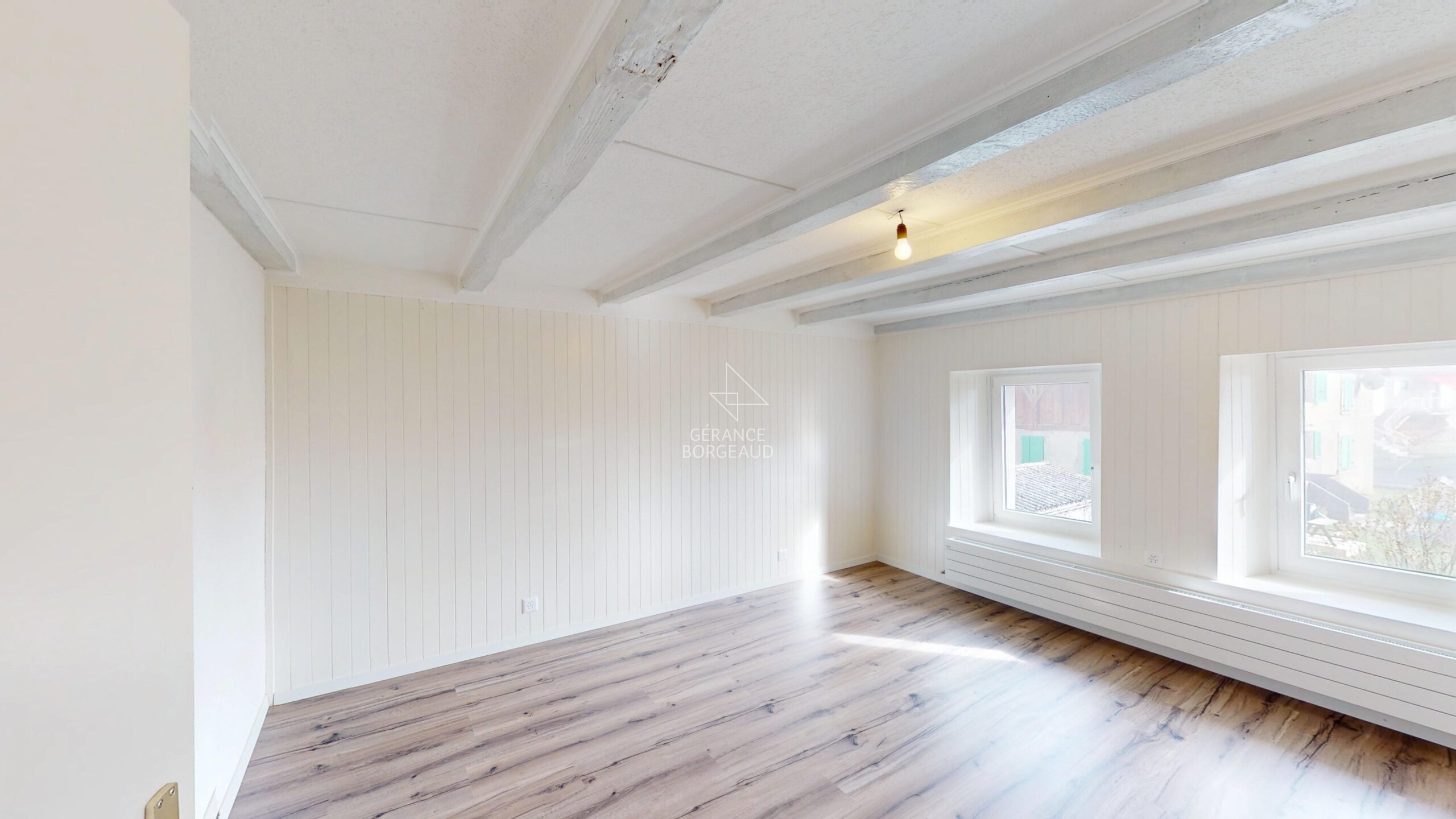 Heller leerer Raum mit Holzboden und sichtbaren Deckenbalken