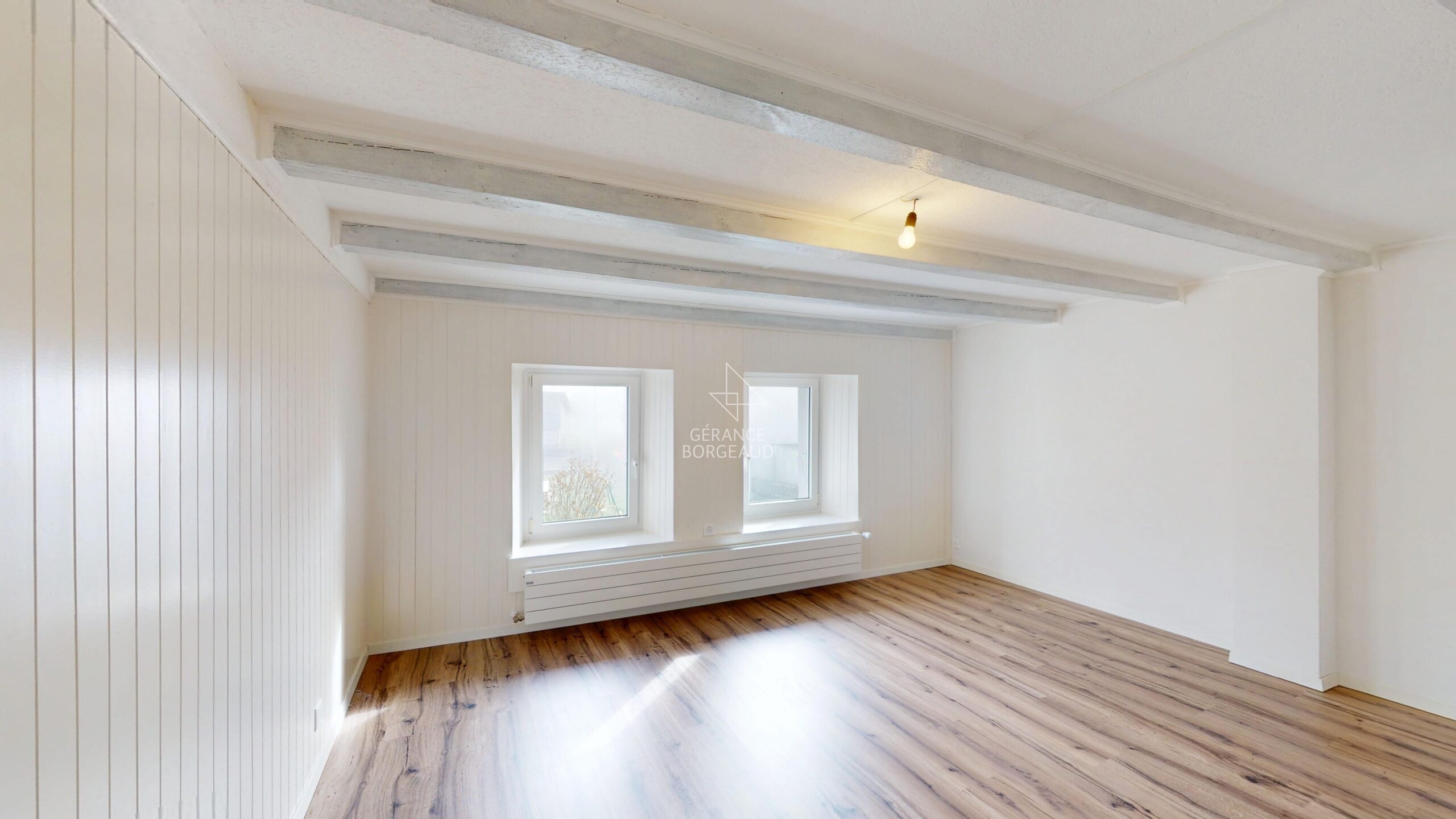 Helles, leeres Zimmer mit Holzoptikboden und sichtbaren Deckenbalken