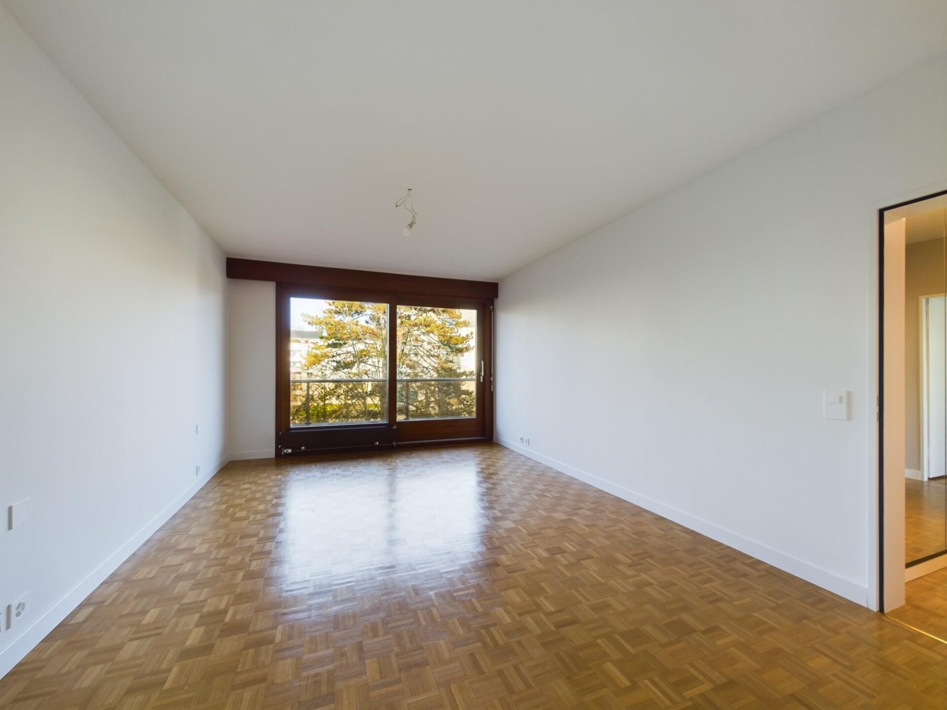 Leerer Wohnraum mit Parkett und Balkonblick