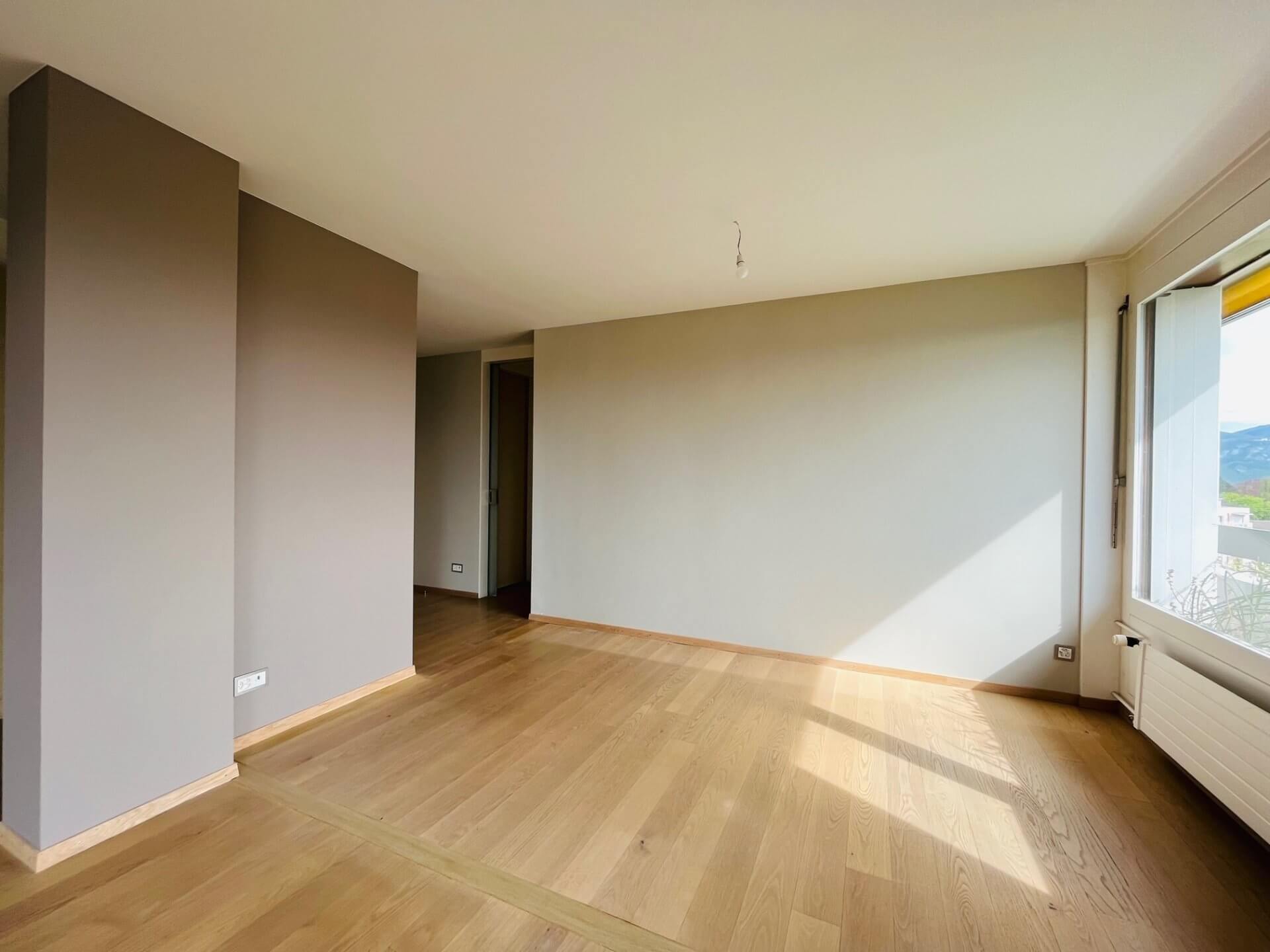 Leerer, heller Wohnraum mit Parkett und Balkonfenster