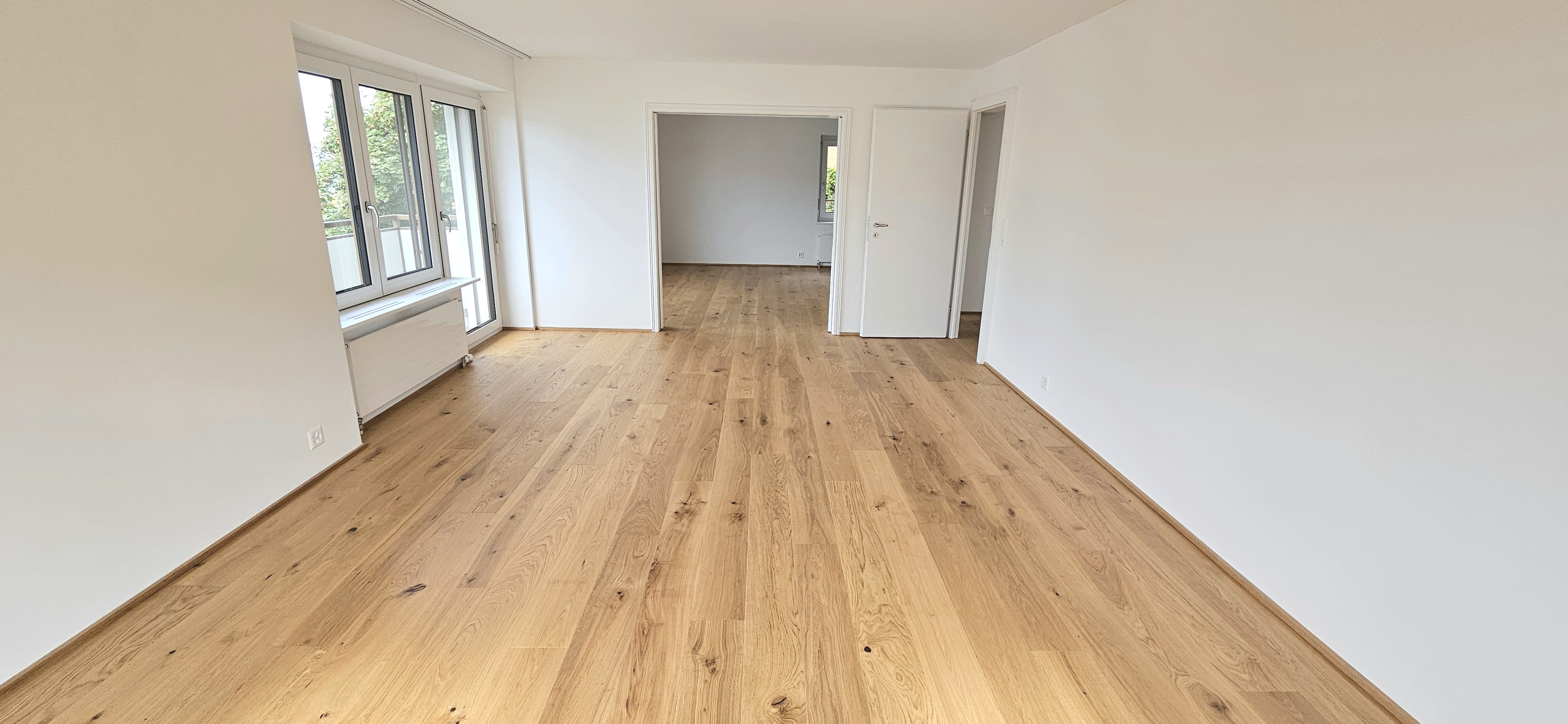 Heller leerer Wohnraum mit Parkett und Balkonfenstern