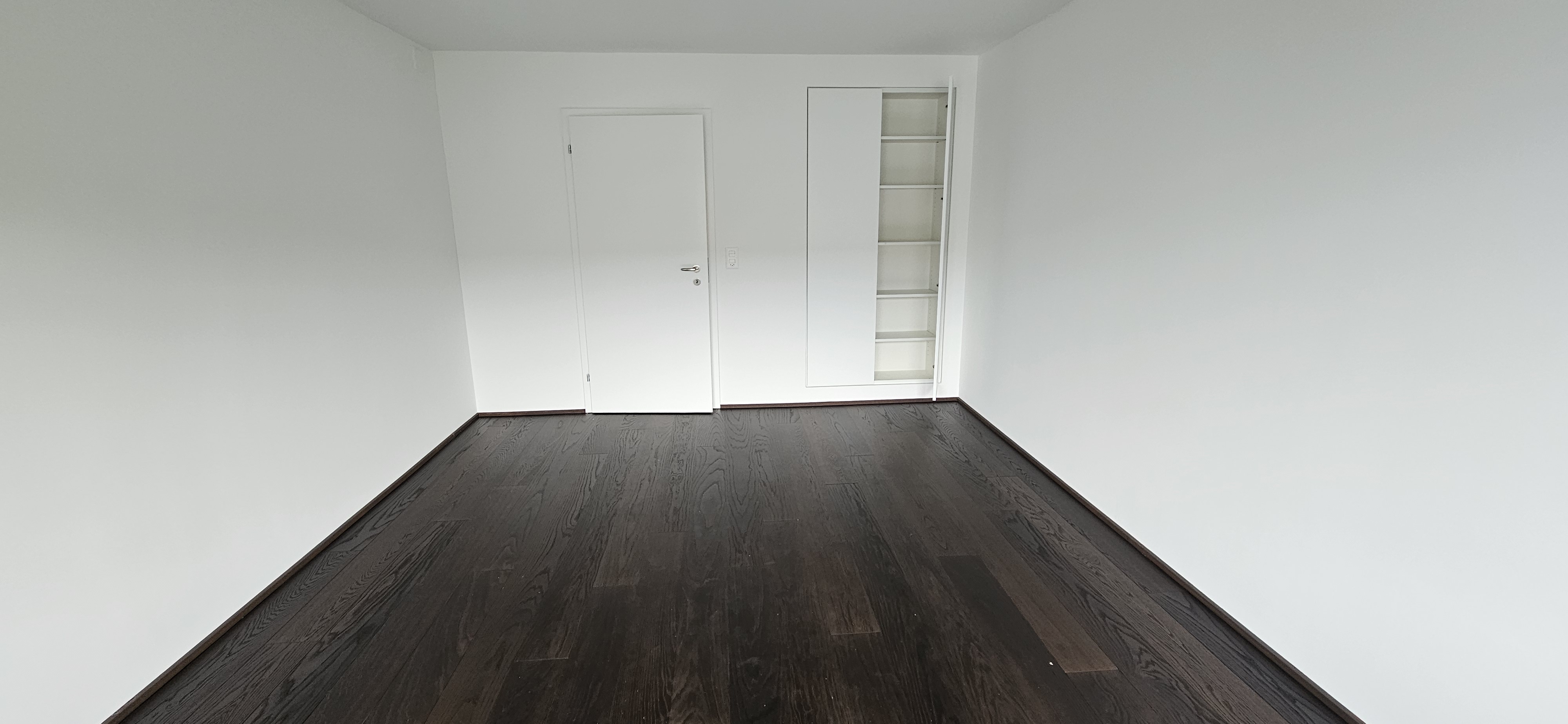 Leerer, frisch renovierter Raum mit dunklem Holzboden