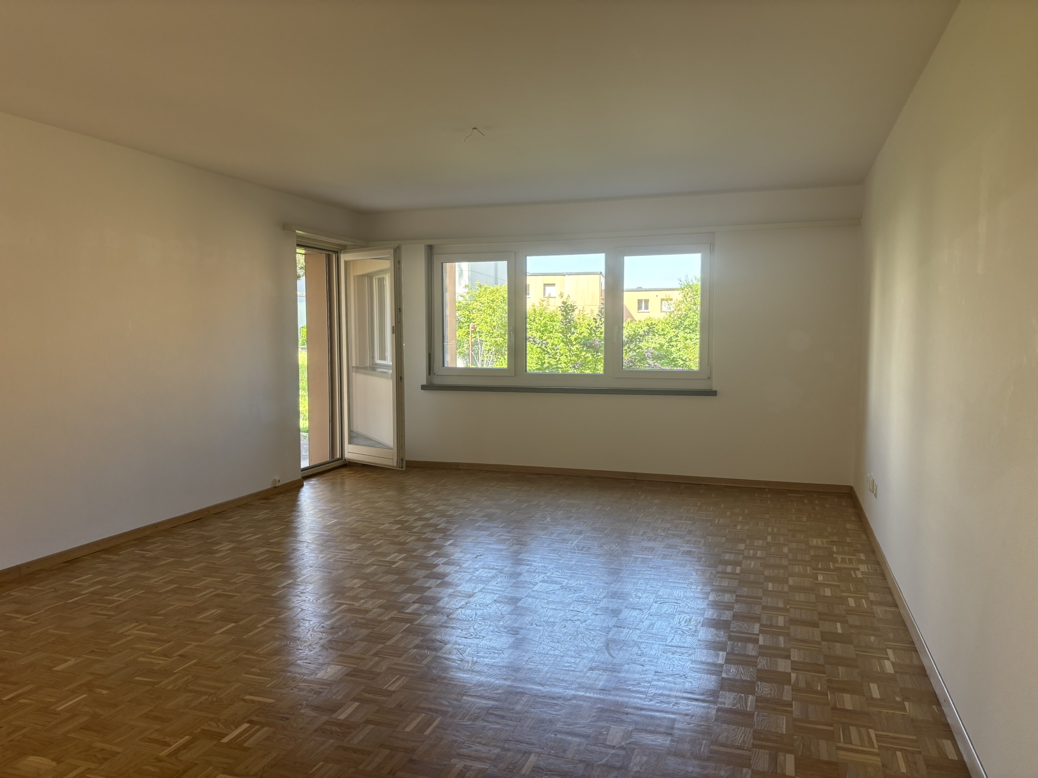 Leerer Wohnraum mit Parkettboden und Fenstern