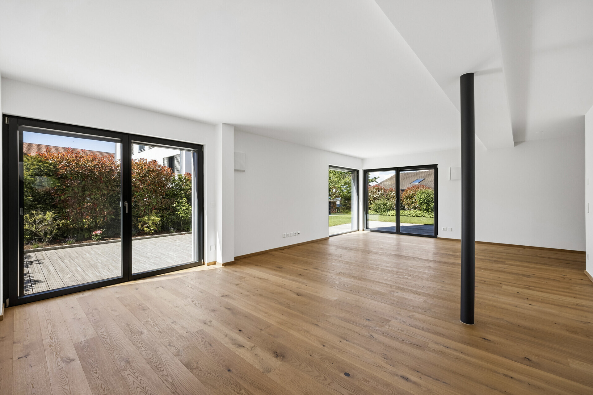 Heller, leerer Wohnraum mit Holzfußboden und großen Fensterflächen