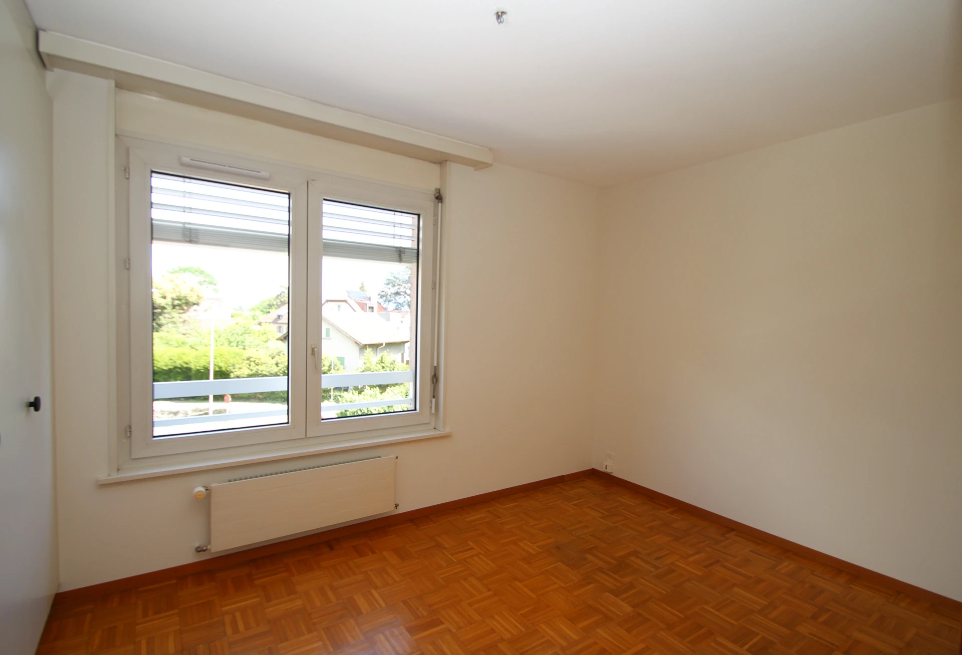 Leerer heller Raum mit Parkettboden und Fenster