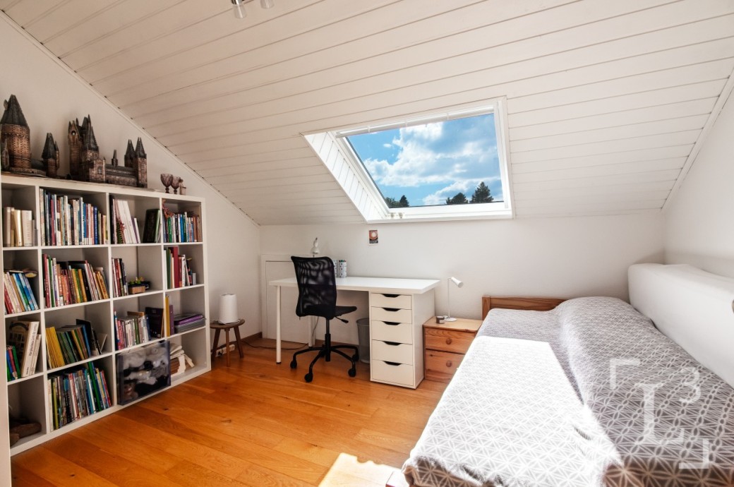 Helles Dachzimmer mit Bett, Schreibtisch und Bücherregal
