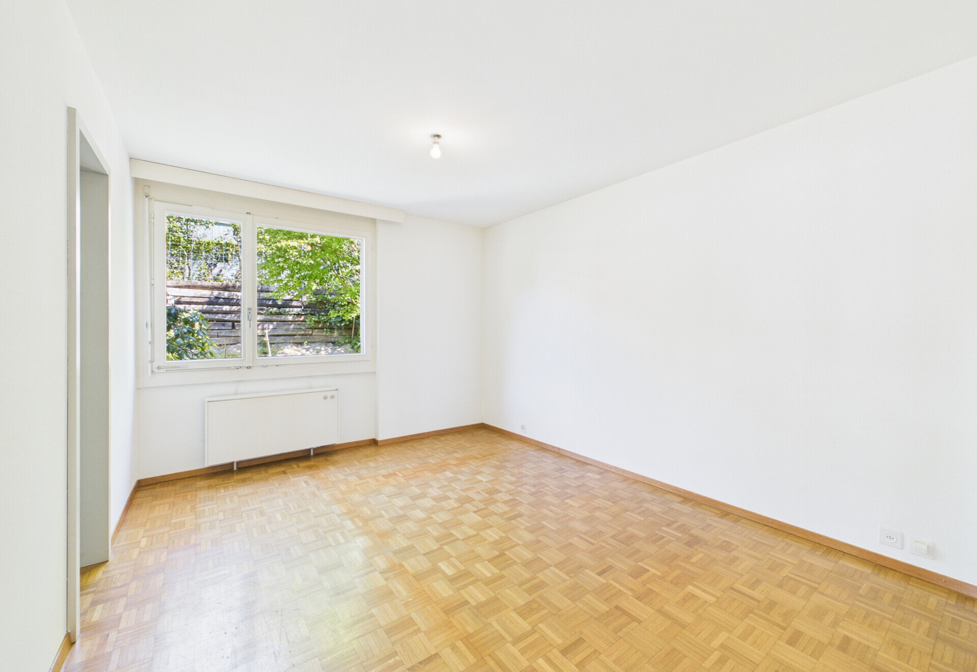 Leerer heller Wohnraum mit Parkett und Fensterblick ins Grüne