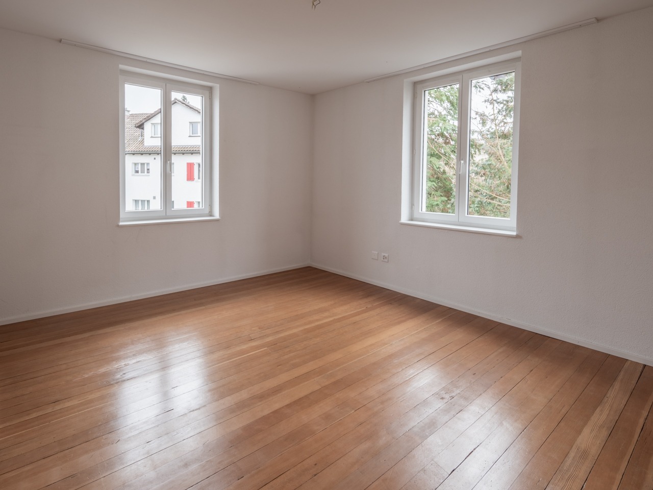 Leeres Zimmer mit Holzboden und zwei Fenstern