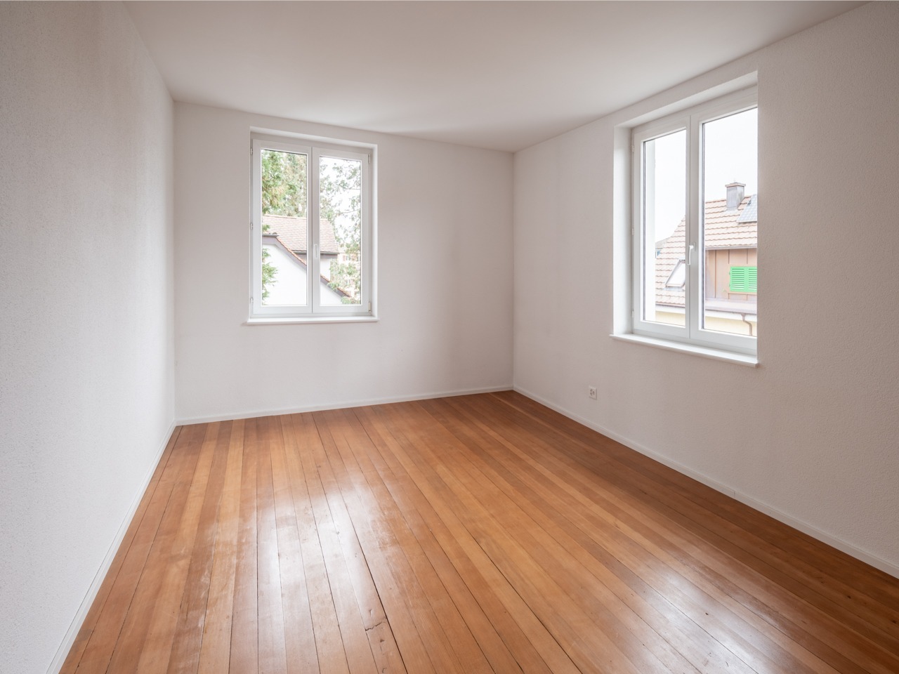 Leerer heller Raum mit Holzboden und zwei Fenstern