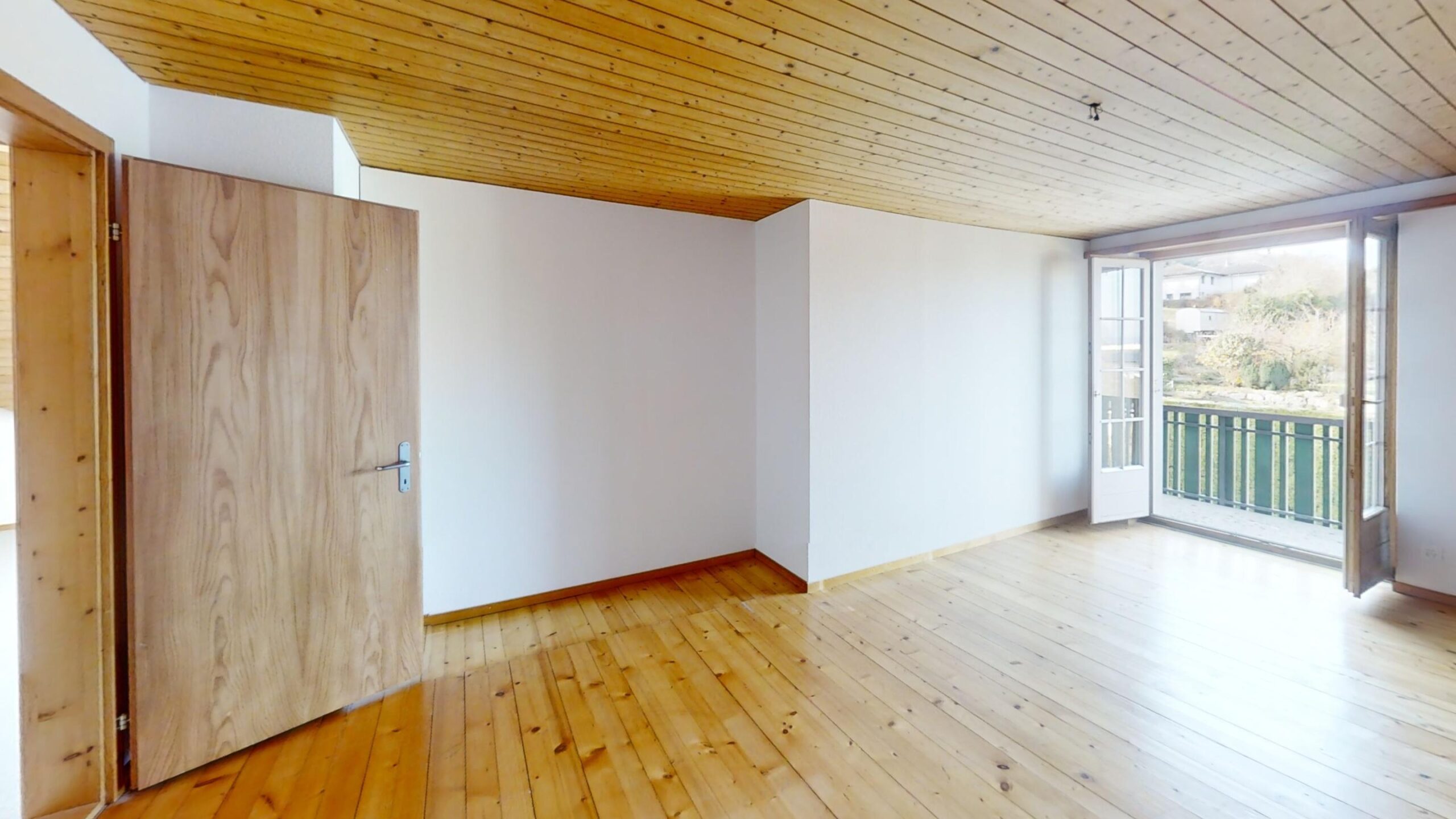 Helles leeres Zimmer mit Holzboden und Balkonzugang