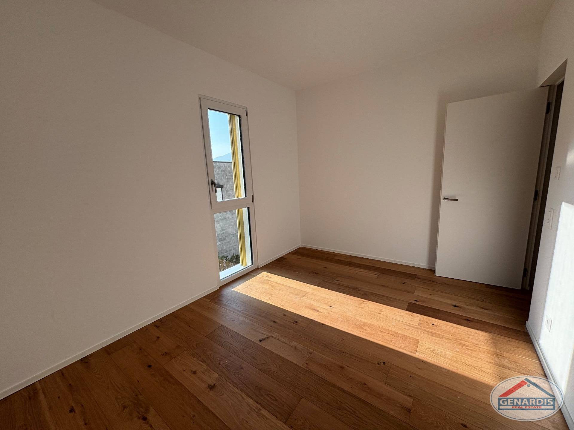 Helles, leeres Zimmer mit Holzboden und schmalem Fenster