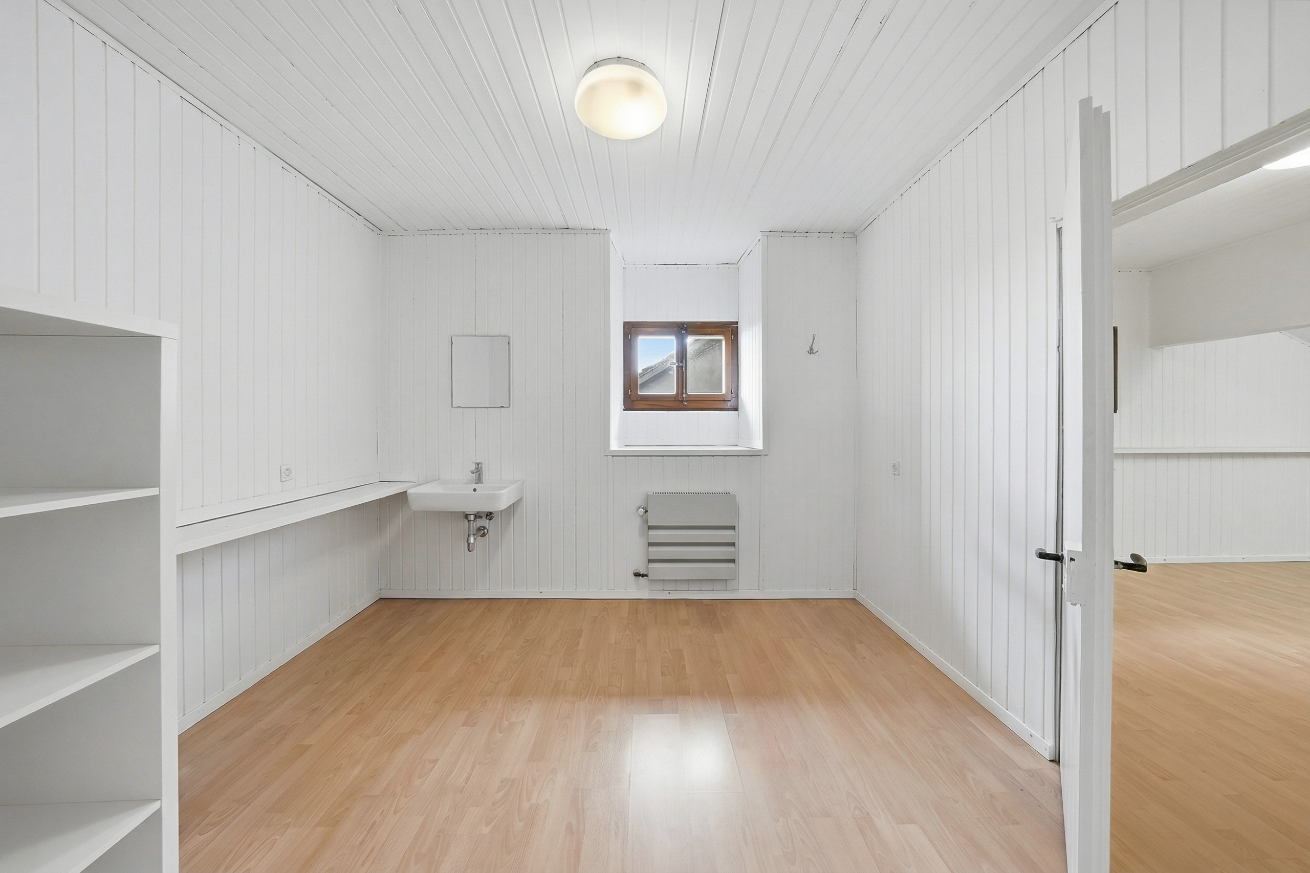 Helles, leerstehendes Zimmer mit weißer Holzverkleidung und Holzboden