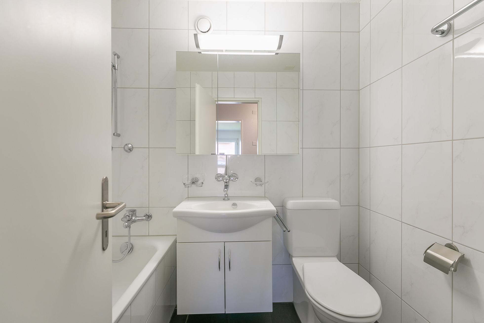 Kleines, modern gefliestes Badezimmer mit Badewanne und WC
