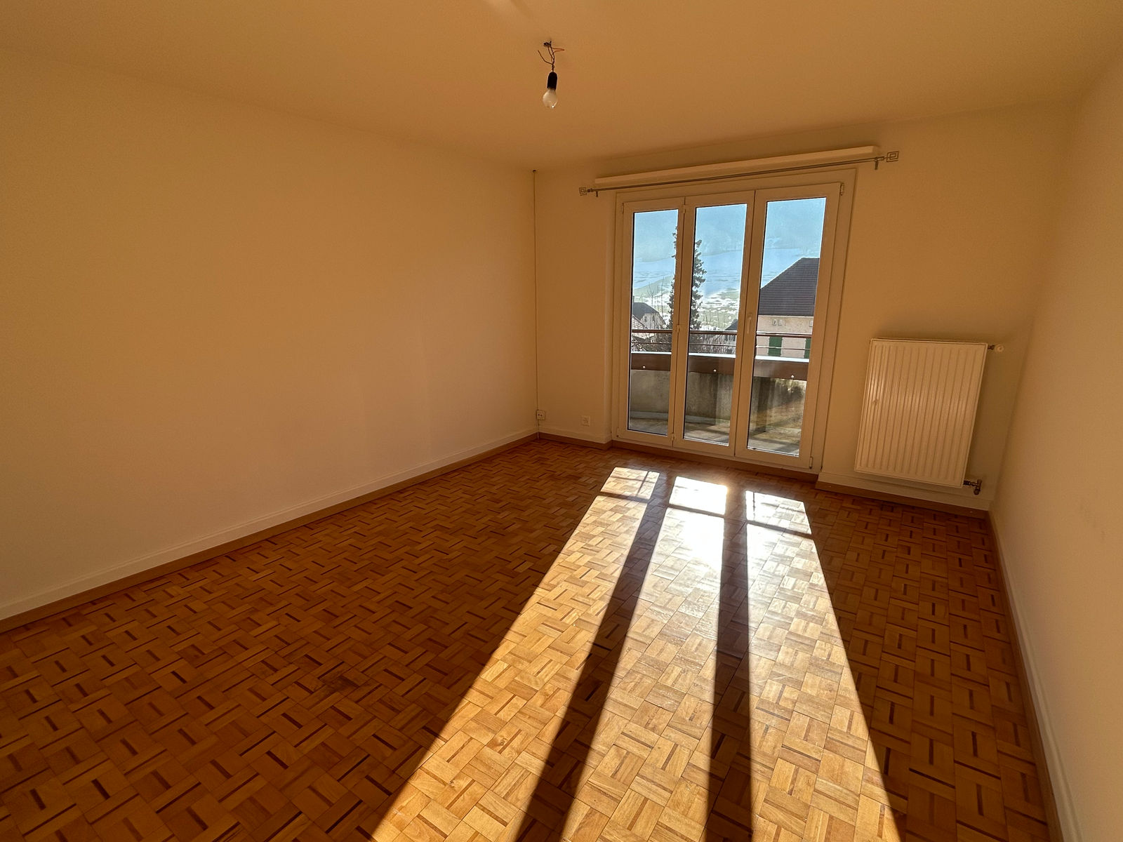 Leerer Wohnraum mit Parkett und Balkonblick
