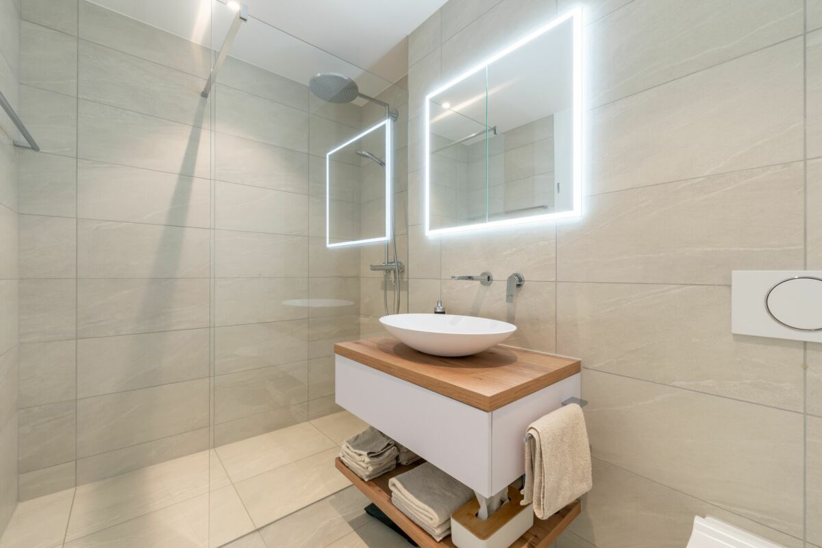 Modernes Badezimmer mit begehbarer Dusche und beleuchtetem Spiegel