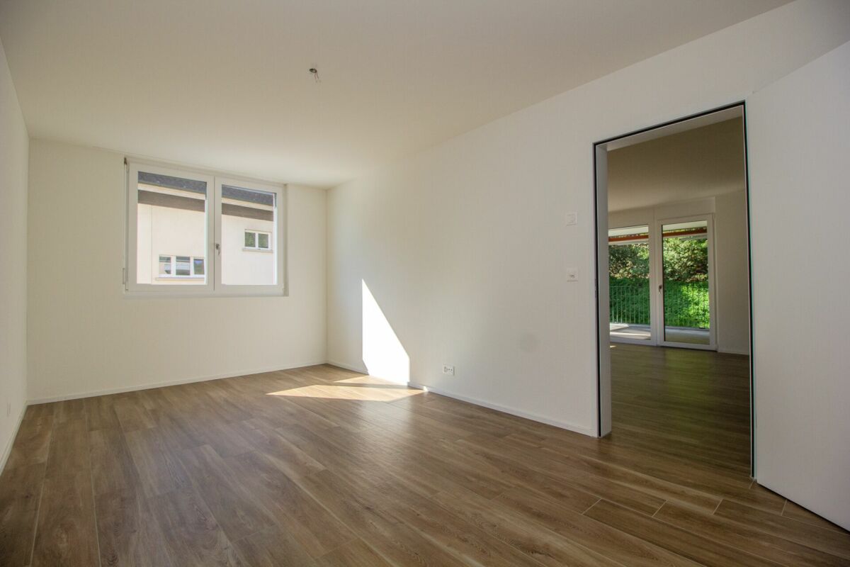 Heller leerer Wohnraum mit Holzoptikboden und Fenster zum Garten