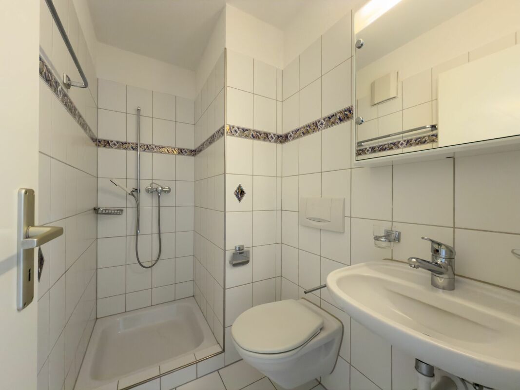 Kleines weiß gefliestes Bad mit Dusche und WC