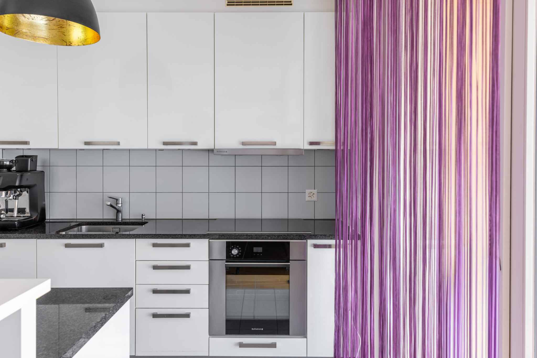 Moderne Küche mit weißen Fronten und lila Vorhang