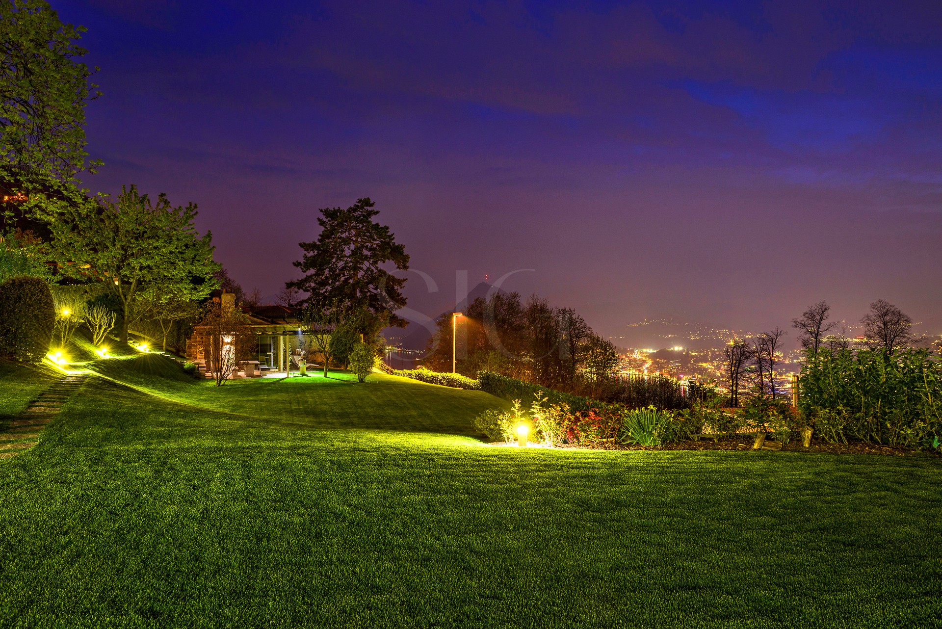 Gepflegter Garten bei Nacht mit Stadtblick