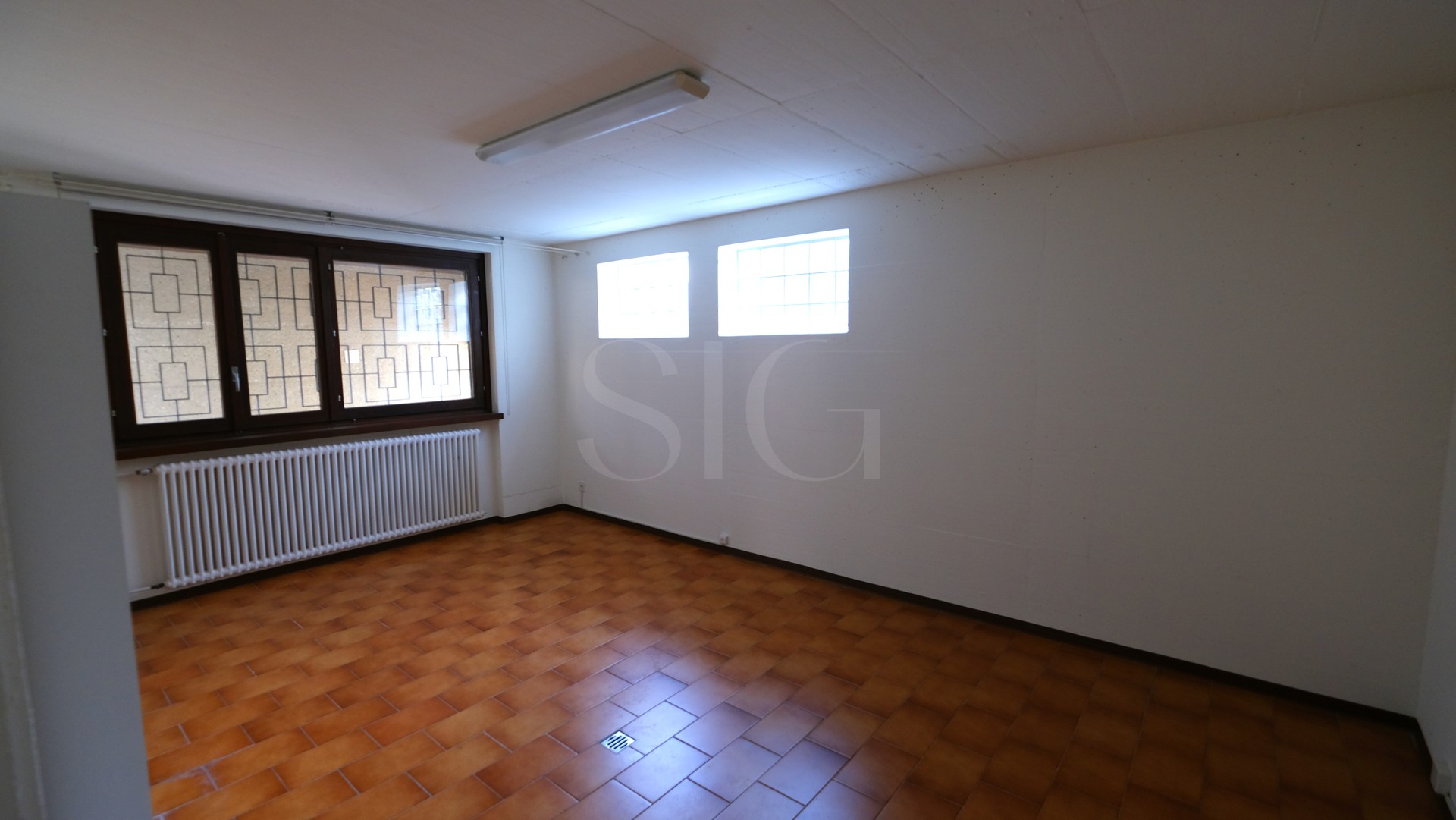 Leerer Wohnraum mit Kachelboden und Fenstern