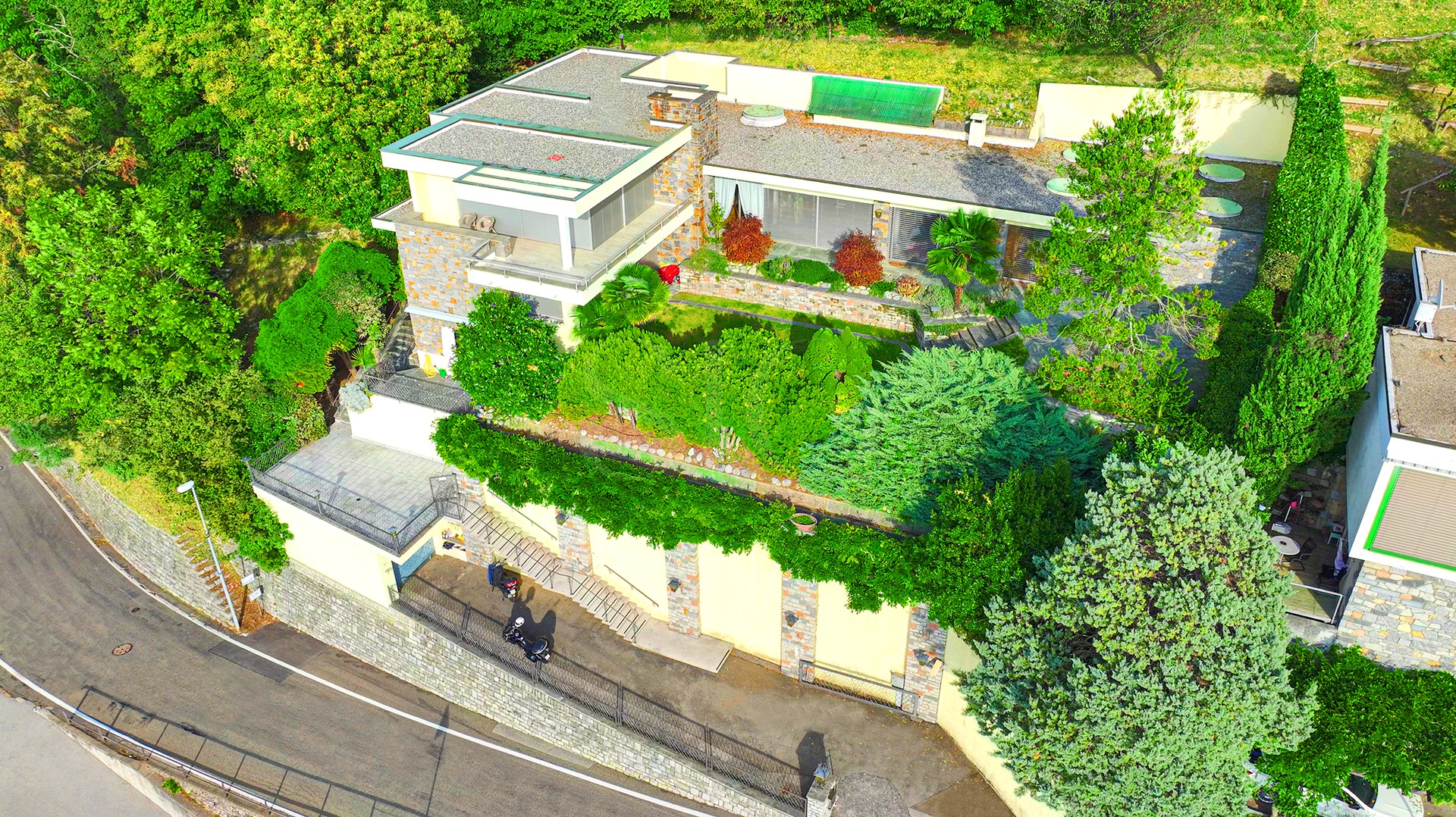 Drohnenansicht eines großzügigen Hauses mit Dachterrasse und üppiger Bepflanzung