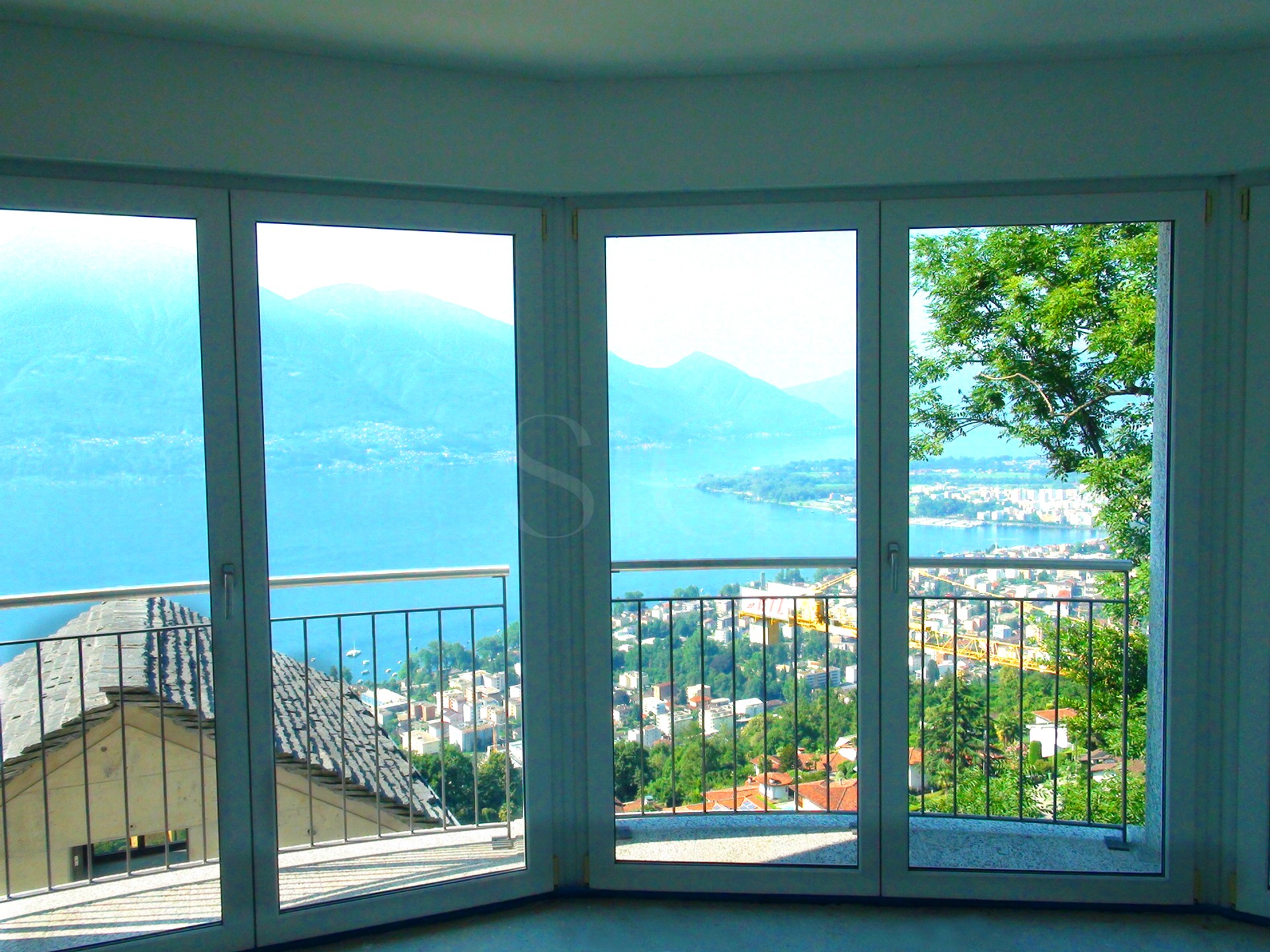 Blick durch große Balkonfenster auf See und Berge