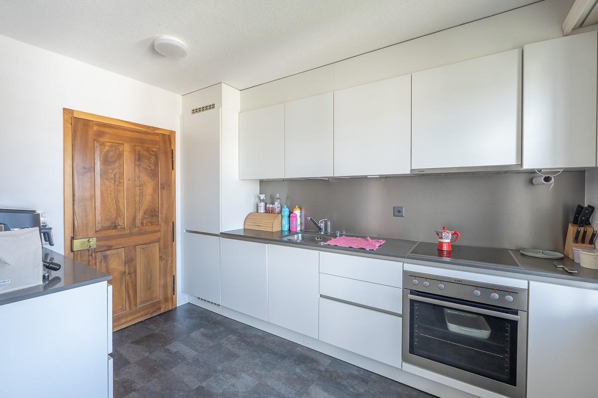 Moderne Küche mit weißen Fronten und Holz­tür