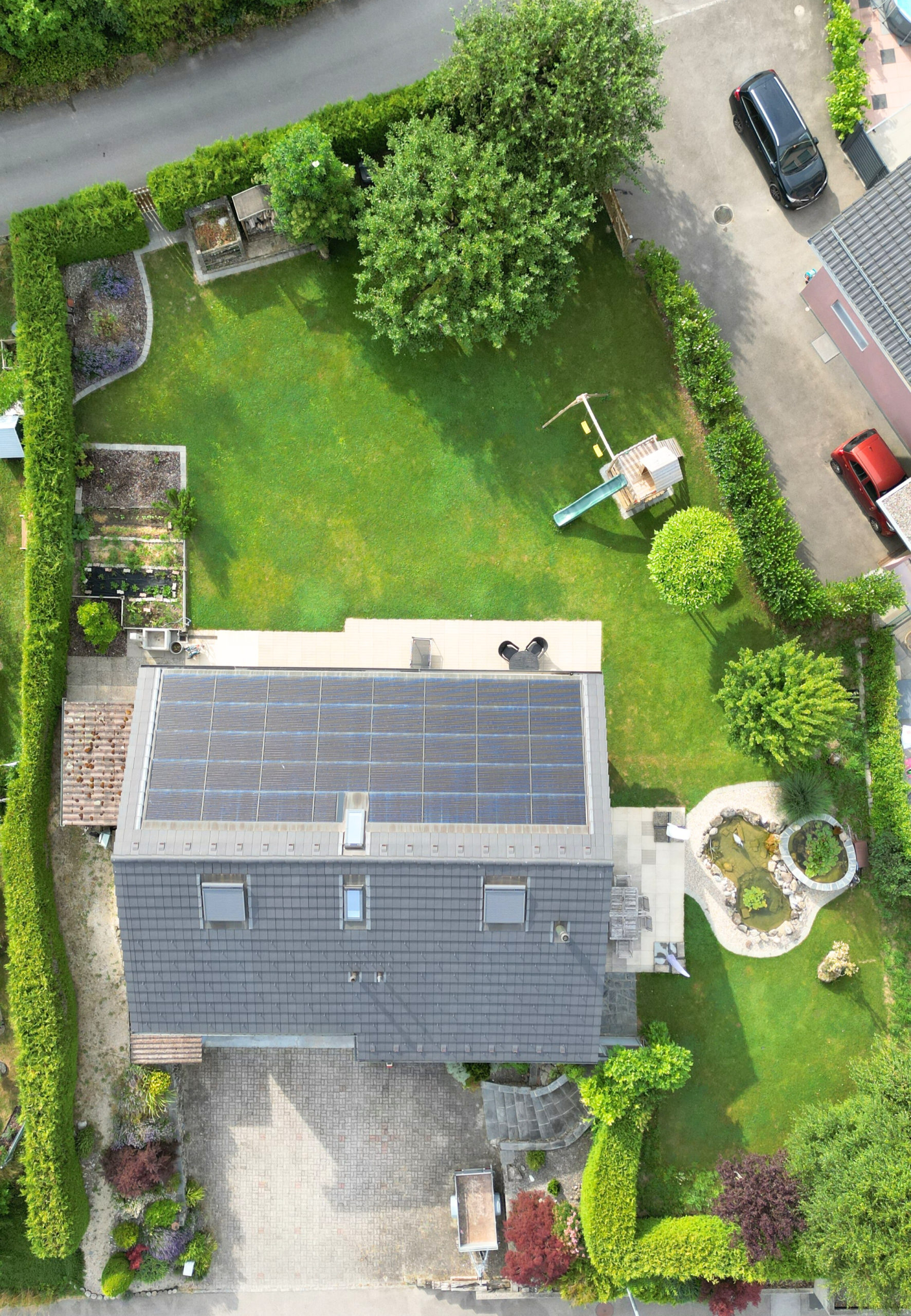 Luftaufnahme eines großen, gepflegten Gartens mit Hausdach und Solarmodulen