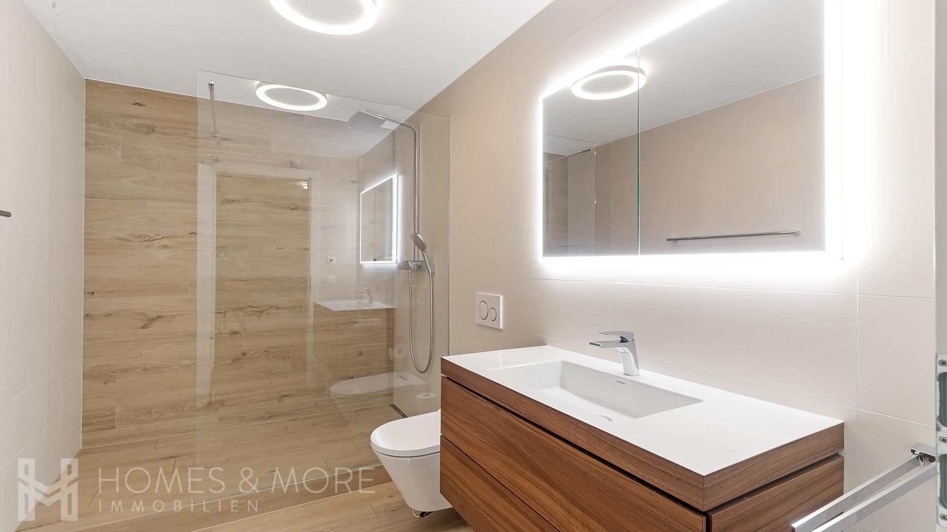 Modernes Badezimmer mit Walk-in-Dusche und beleuchtetem Spiegel