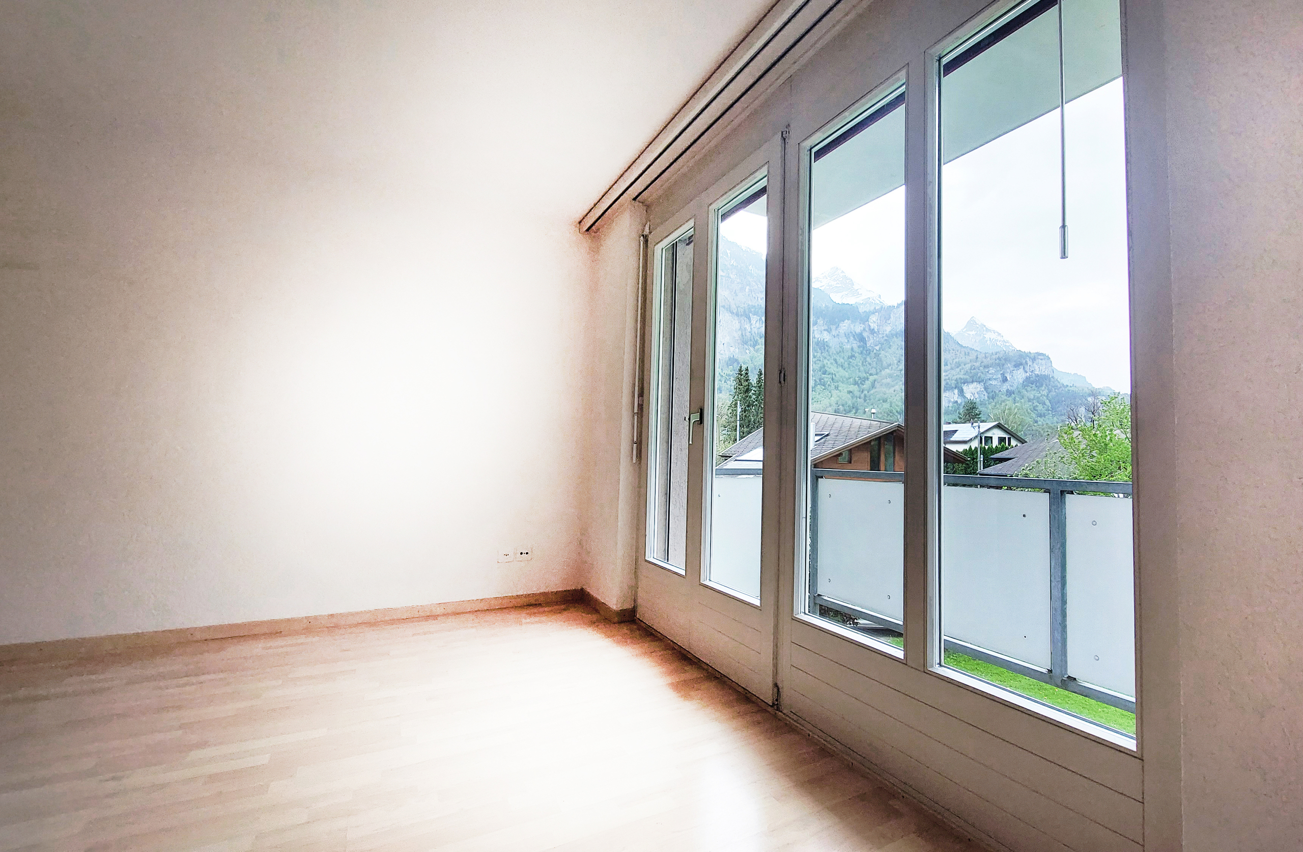 Heller leerer Raum mit großer Fensterfront und Bergblick