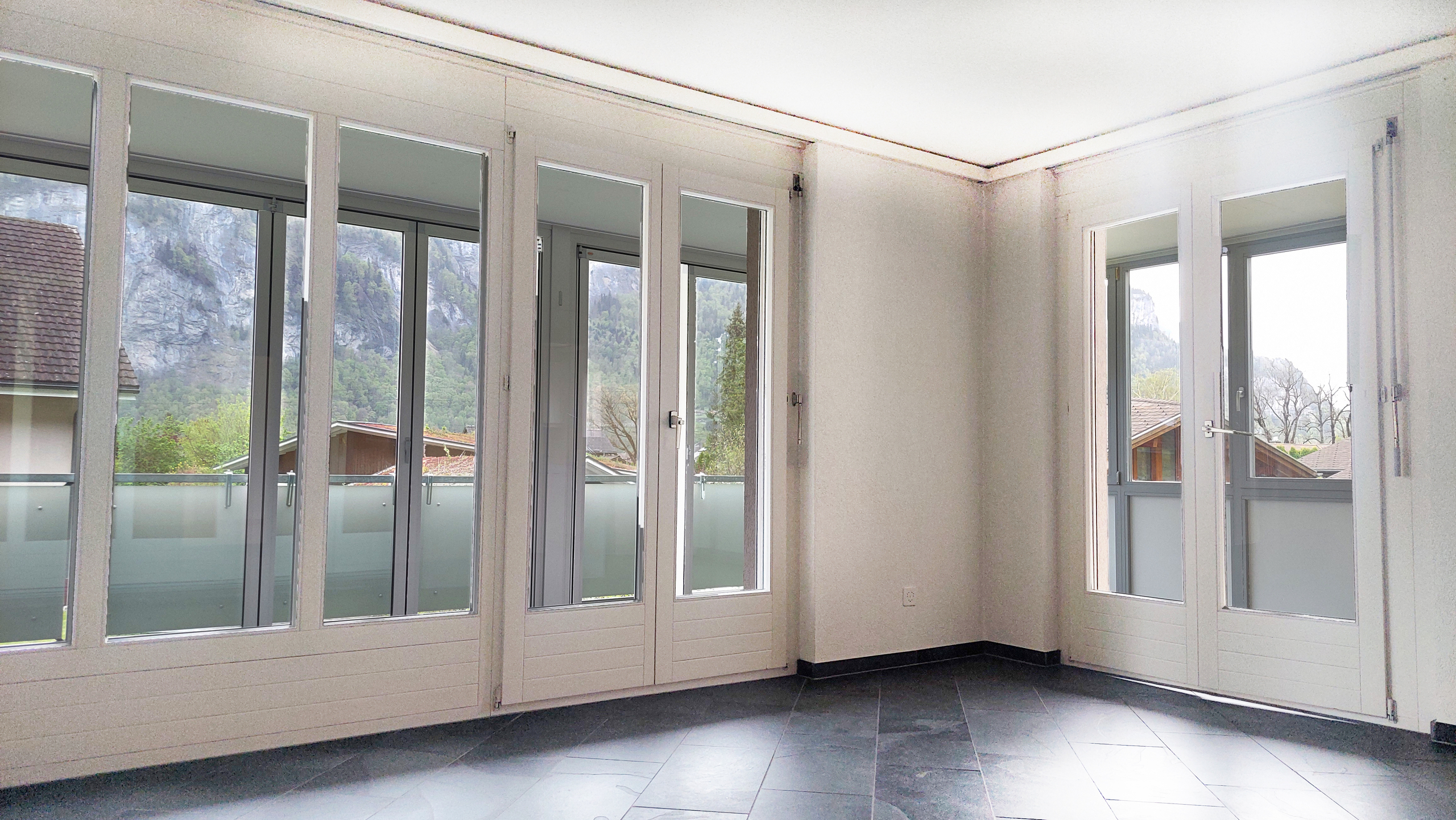Heller, leerer Raum mit großer Fensterfront und Bergblick