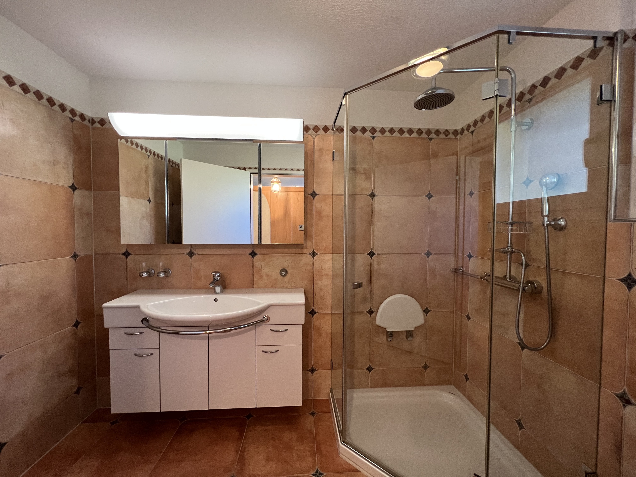 Badezimmer mit orangefarbenen Fliesen und Glasdusche