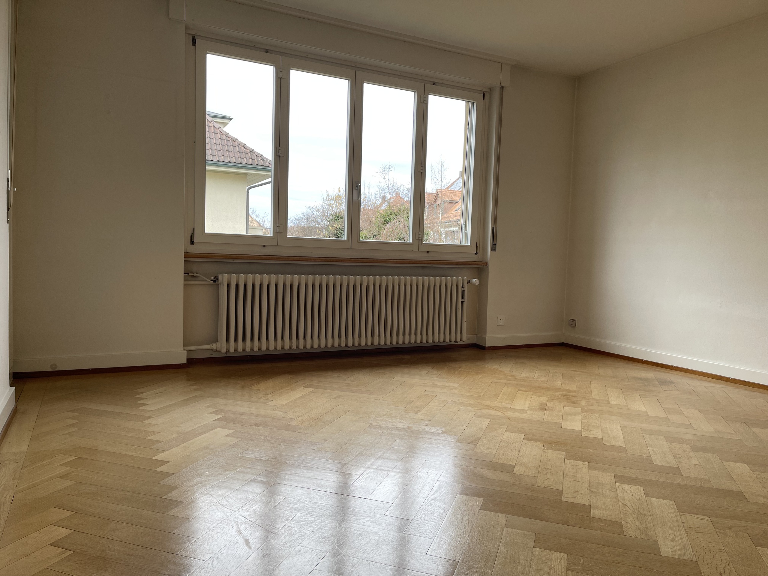 Leerer Raum mit Fischgrätparkett und großem Fenster