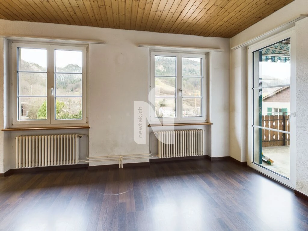 Leerer Wohnraum mit Holzdecke und Balkonzugang