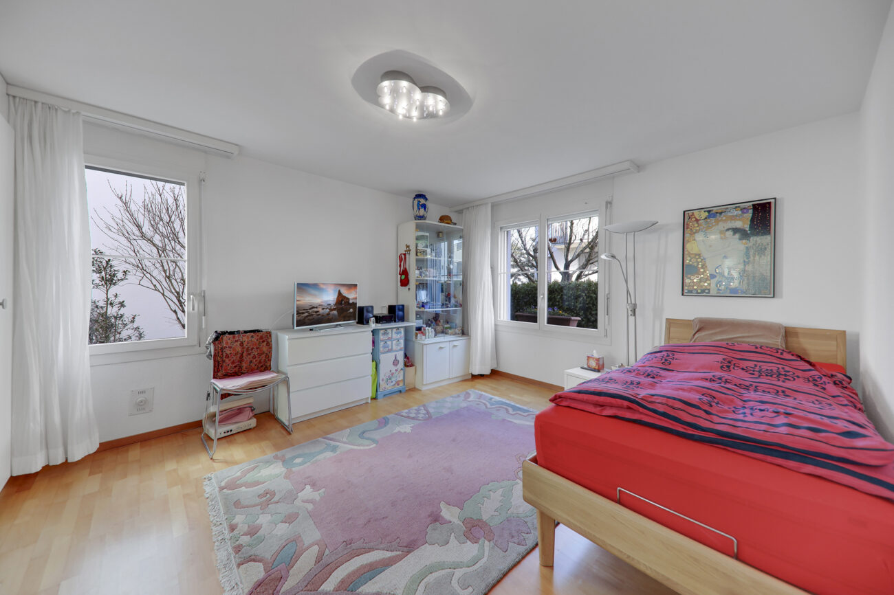 Helles Schlafzimmer mit zwei Fenstern und schlichter Einrichtung